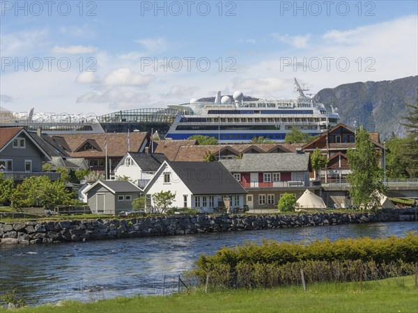 A riverside village with a large cruise ship in the background, surrounded by mountains under a
