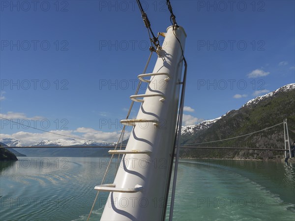 View from the deck of a ship with a view of mountains and a bridge over the water under a clear
