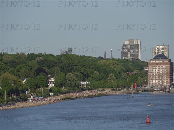 Shoreline landscape with a long beach and many people, surrounded by green nature, Elbe, Hamburg,