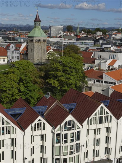 View of a city with a tower, modern buildings and a green treetop under a cloudy sky, Stavanger,