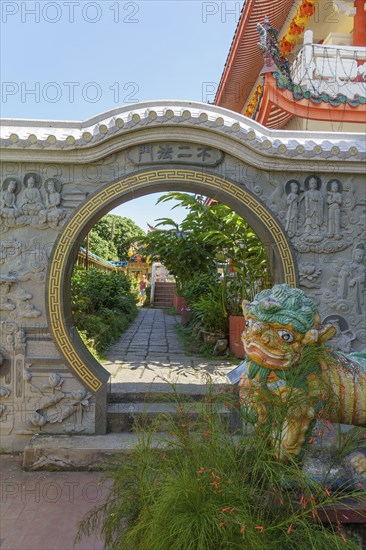 A decorative stone arch with a sculpture of a lion in a traditional temple garden with surrounding