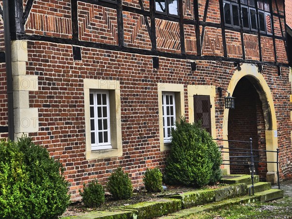 The entrance of a half-timbered house with brick walls, white windows and green bushes, asbeck,