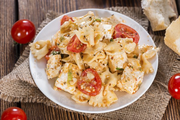 Portion of Pasta Salad with Farfalle, Cheese and Tomatoes (on wooden background)