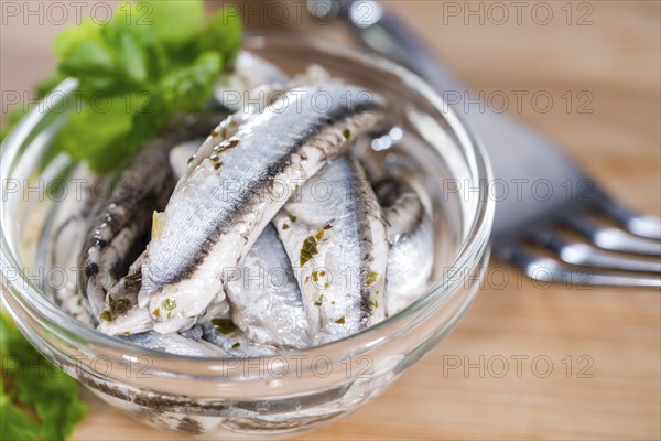 Pickled Anchovis with herbs (close-up shot) on wooden background