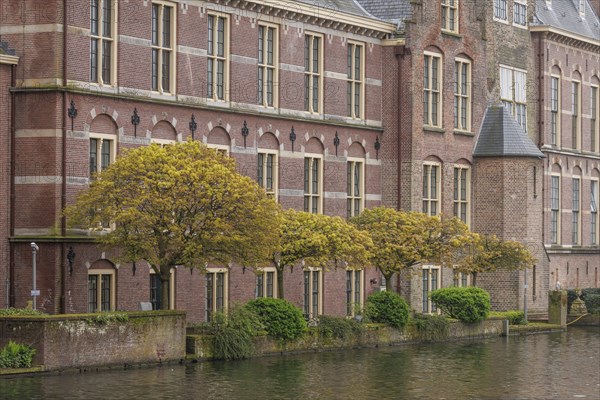 A historic brick faÃ§ade with many windows, lined with trees and close to a body of water, The
