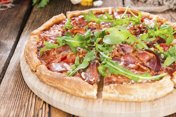 Fresh made Ham Pizza with rocket, tomatoes, garlic and cheese on wooden background