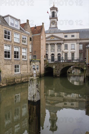 Historic buildings and bridge with clock tower over a quiet canal, reflecting in the water,
