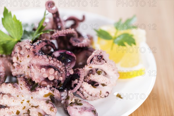 Portion of Octopus Salad (with fresh herbs and garlic) on wooden background