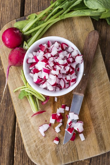 Bowl with diced Radishes (selective focus, close-up shot) on wooden background