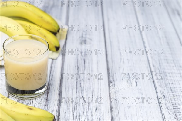 Glass of Banana Juice (close-up shot) on wooden background