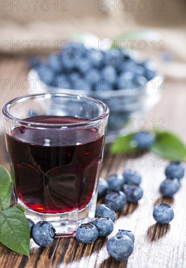 Blueberry Liqueur in a shot glass (on wooden background)