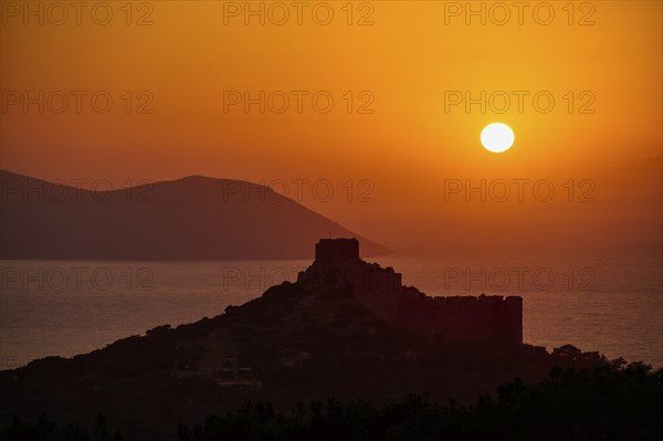 Castle ruins in silhouette against a dramatic sunset over the sea and mountains, Kritinia Castle,