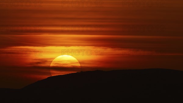 A dramatic sunset behind a hill that bathes the sky in deep red-orange tones, offshore island,