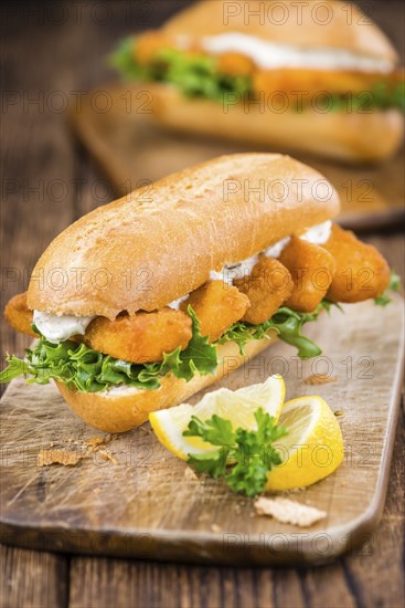 Roll with fried Fish Sticks (close-up shot) on an old wooden table