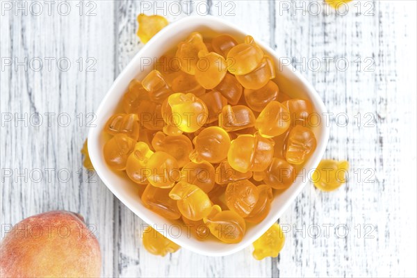 Gummy Peaches (close-up shot) with some fresh fruits on wooden background