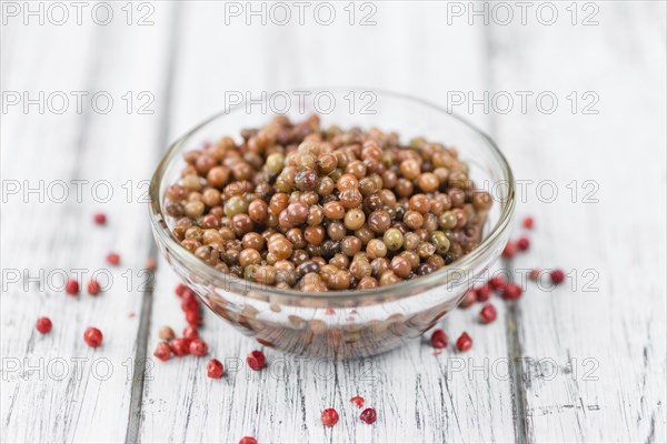 Preserved Pink Peppercorns on an old wooden table as detailed close-up shot, selective focus