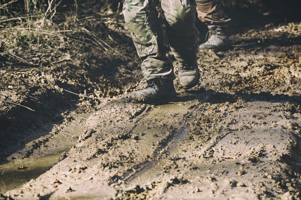 Brown military boots on mud, dirt and puddle