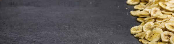 Some Dried Banana Chips on a slate slab as detailed close-up shot, selective focus