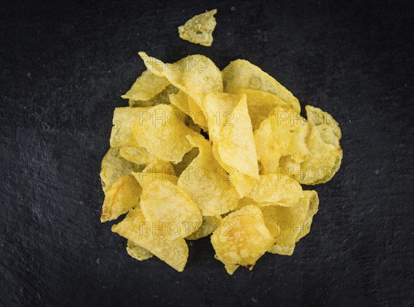 Portion of Cheese and Onion Potato Chips as detailed close up shot on a slate slab (selective