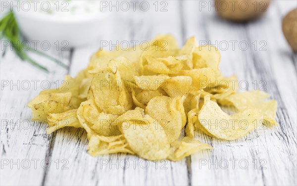 Potato Chips (Sour Cream taste) on rustic wooden background (close-up shot)