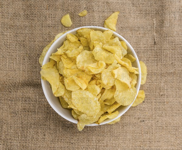 Potato Chips (Sour Cream taste) on a vintage background as detailed close-up shot (selective focus)