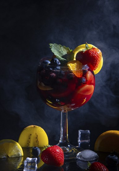 Fruity cocktail in a wine glass, with fresh strawberries, blueberries and oranges, against a dark