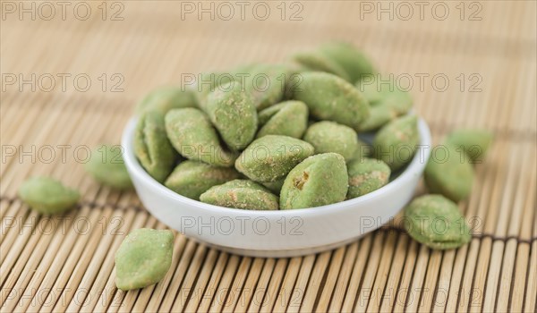 Wasabi coated Peanuts as high detailed close-up shot on a vintage wooden table (selective focus)
