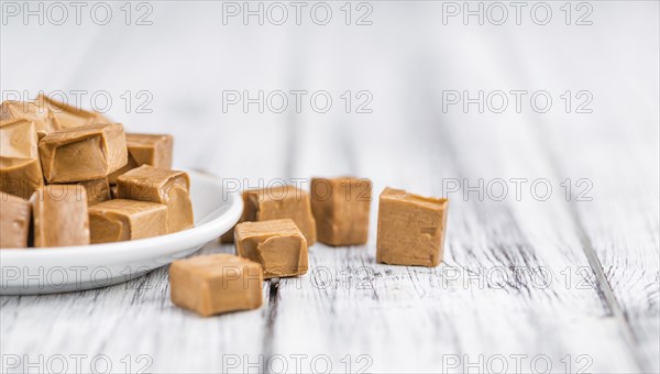 Caramel pieces as high detailed close-up shot on a vintage wooden table (selective focus)