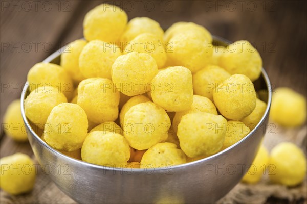 Cheese Balls (fried) as high detailed close-up shot on a vintage wooden table (selective focus)