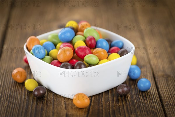 Cocolate coated Peanuts on rustic wooden background (close-up shot)