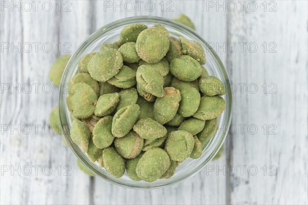 Wasabi coated Peanuts as high detailed close-up shot on a vintage wooden table (selective focus)