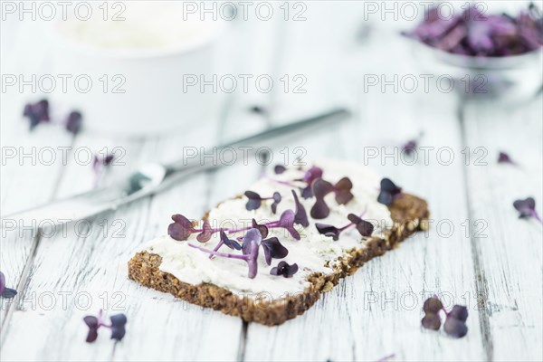 Slice of wholemeal bread with fresh cutted cress and cream cheese on an old wooden table (selective