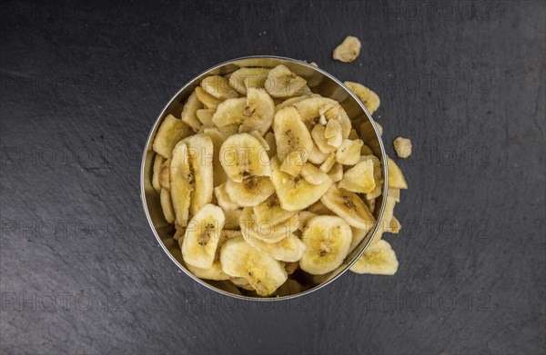Some Dried Banana Chips on a slate slab as detailed close-up shot, selective focus