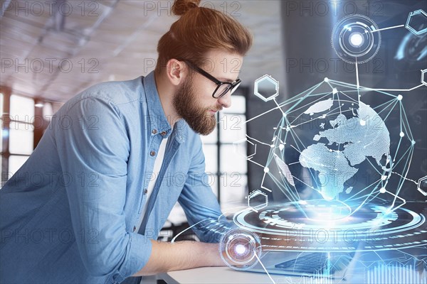 A man in a modern office works on a laptop with a holographic globe and technological graphics in