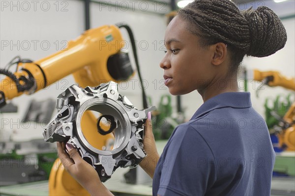 Young woman looking at a machine part in a workshop, a robot arm in the background, AI and