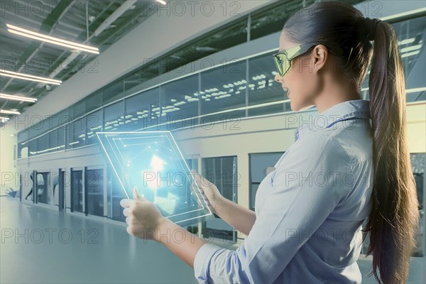 Woman in modern laboratory setup with tablet, surrounded by holographic representations and
