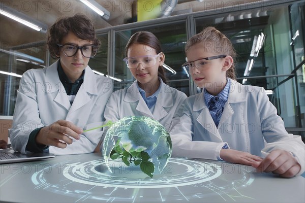 Young scientists in white coats look at a holographic projection of a globe with plants in the