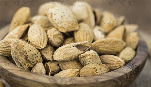 An old wooden table with roasted Almonds (in the shell) as detailed close-up shot (selective focus)