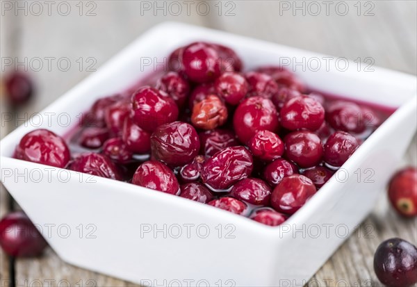 Old wooden table with fresh Preserved Cranberries (close-up shot, selective focus)