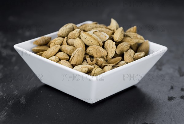 Portion of roasted Almonds (in the shell) on a dark slate slab as detailed close-up shot (selective