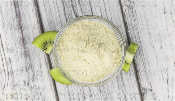 Bowl with fresh made Kiwi powder (close-up shot, selective focus) on an old wooden table