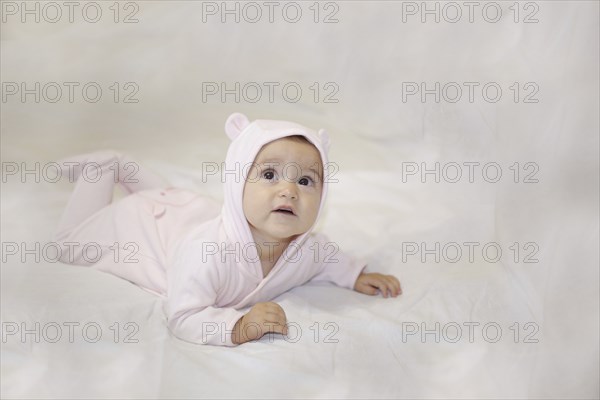 Baby in pink costume with ears hood, laying on a white background looking up