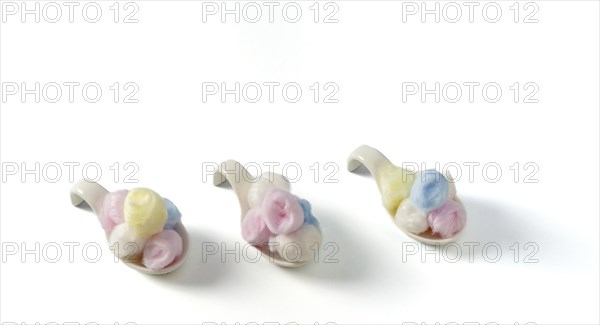 Cotton balls of different colors on white ceramic spoons on a white background