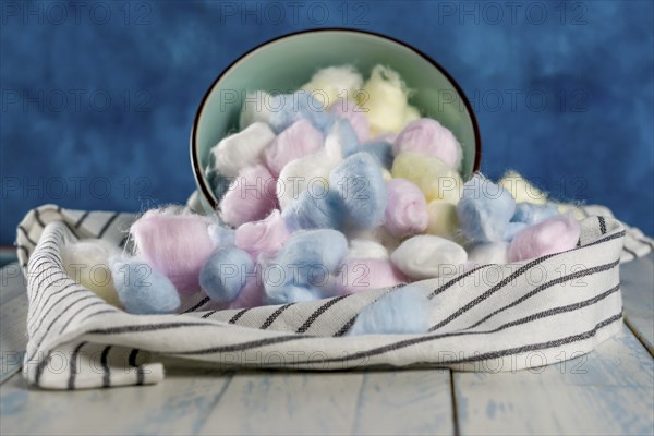 Cotton balls of different colors in a ceramic bowl on a blue background