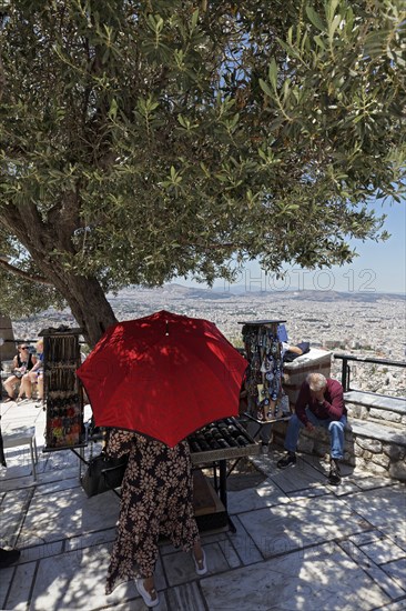 Souvenir stand under a shady olive tree, woman with parasol, panoramic terrace on Lycabettus Hill,