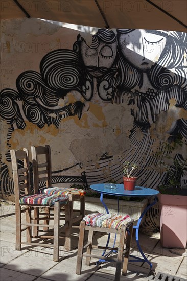 Chairs and table in front of a wall with graffiti, taverna in the old town district of Plaka,