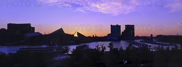 A dramatic and beautiful panoramic sunrise with buildings and boats in silhouette reflected in the