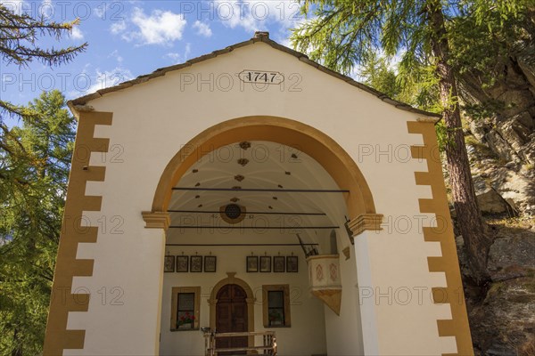 Historic church from 1747 in white colour, surrounded by forest and mountains under a clear sky,