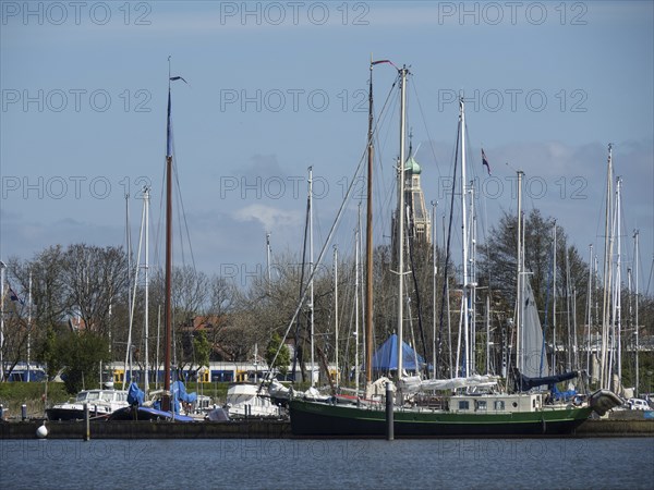 View of a harbour with sailing boats and a historic bell tower in the background, calm water,