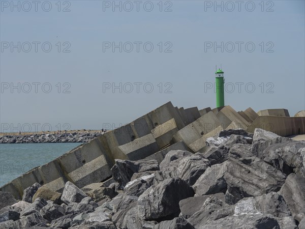Stable rock formations and a green lighthouse at the breakwater along the coast under a clear sky,